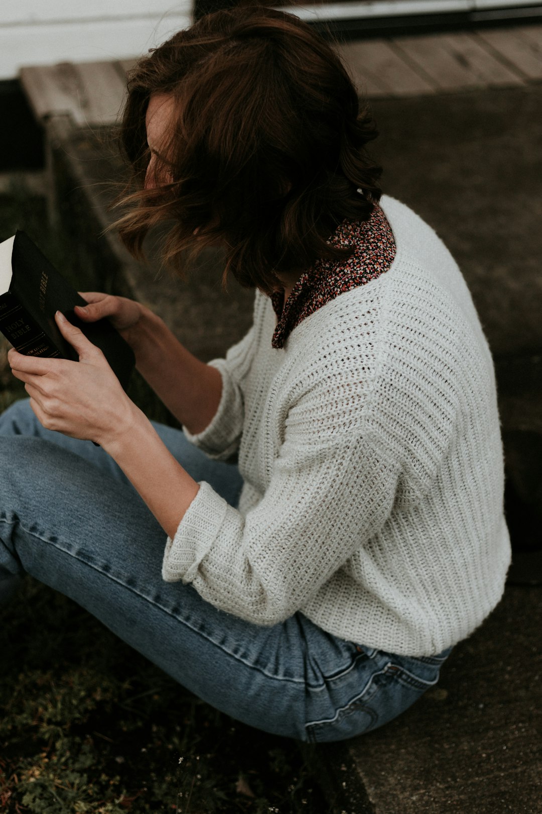 woman-holding-book-sitting-on-brown-concrete-pathway-hssmuggje98